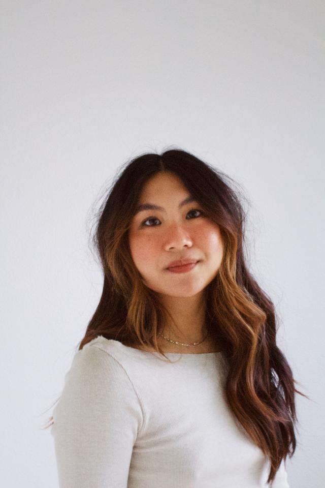 Person with long brown hair wearing white shirt against a white backdrop