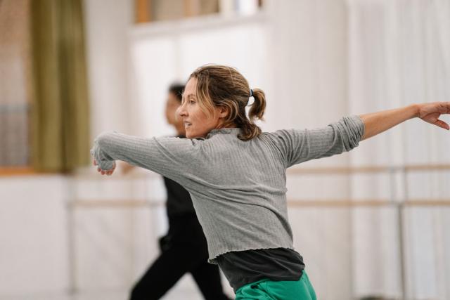 person in green pants and grey top moving arms agains a white background