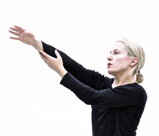 person in black shirt with blonde hair reaching arms out on a diagonal