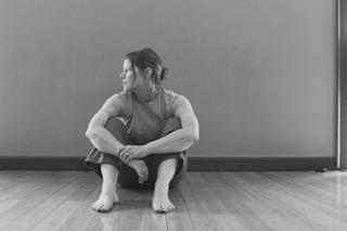 a black & white image of a woman sitting on the floor with their arms over their legs and looking profile 