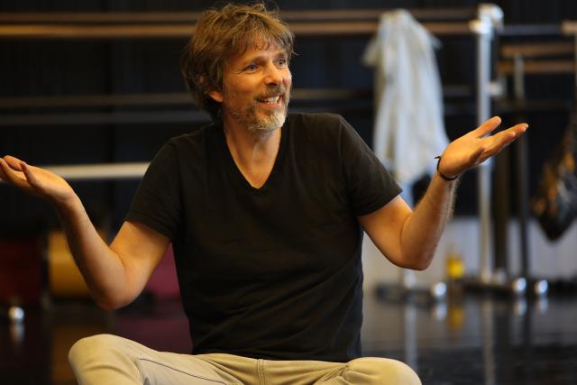 an image of a man with scruffy brown and grey facial hair sitting criss crossed with his hands open like they're holding trays