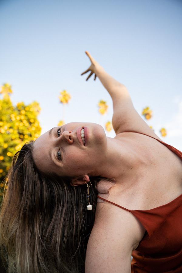 dancer with long blonde hair leaning to the side and reaching towards the sky with yellow flowers and a red dress