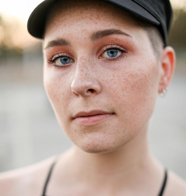 artist looking at camera with black top and black hat and shaved head