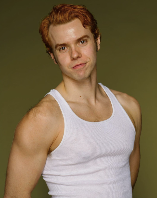 image of adrian wearing a white tanktop looking into the camera with an olive green background