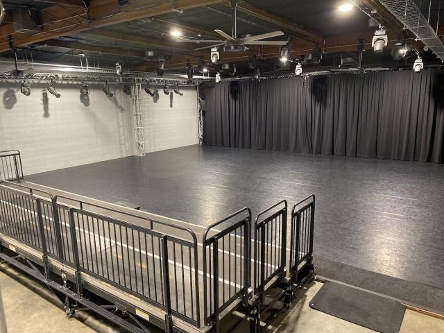 large space with black floors, grey walls, black curtain, and seating risers at the front