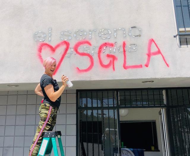 person on top of green ladder spray painting letters on a building