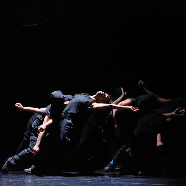 Dancers leaning back in a circle under a pool of light