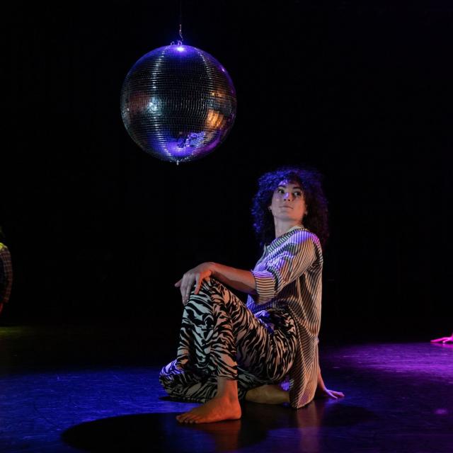 Three dancers kneel beneath disco balls in black and white costumes and purple, blue and yellow light