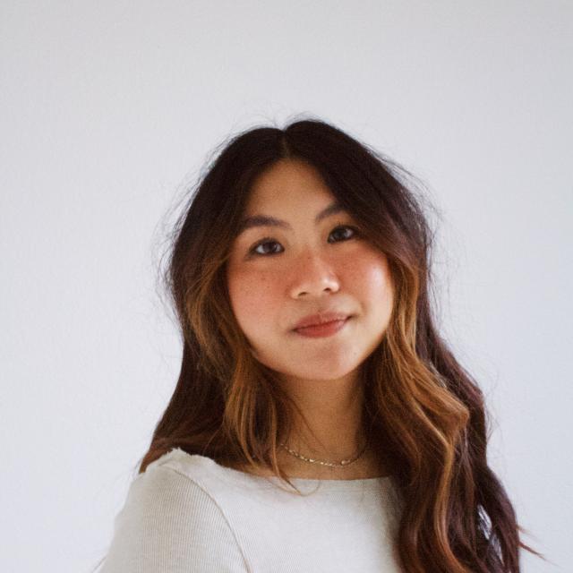 Person with long brown hair wearing white shirt against a white backdrop